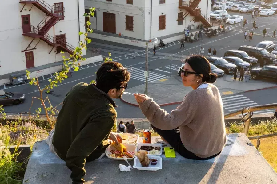 Una coppia cena all'aperto al Fort Mason Center di San Francisco. La donna offre al suo compagno un assaggio di cibo.